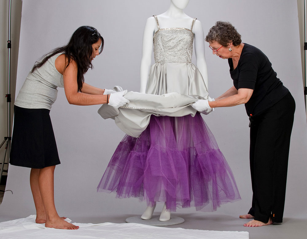 two women dressing a mannequin. Click to view the detail of this image